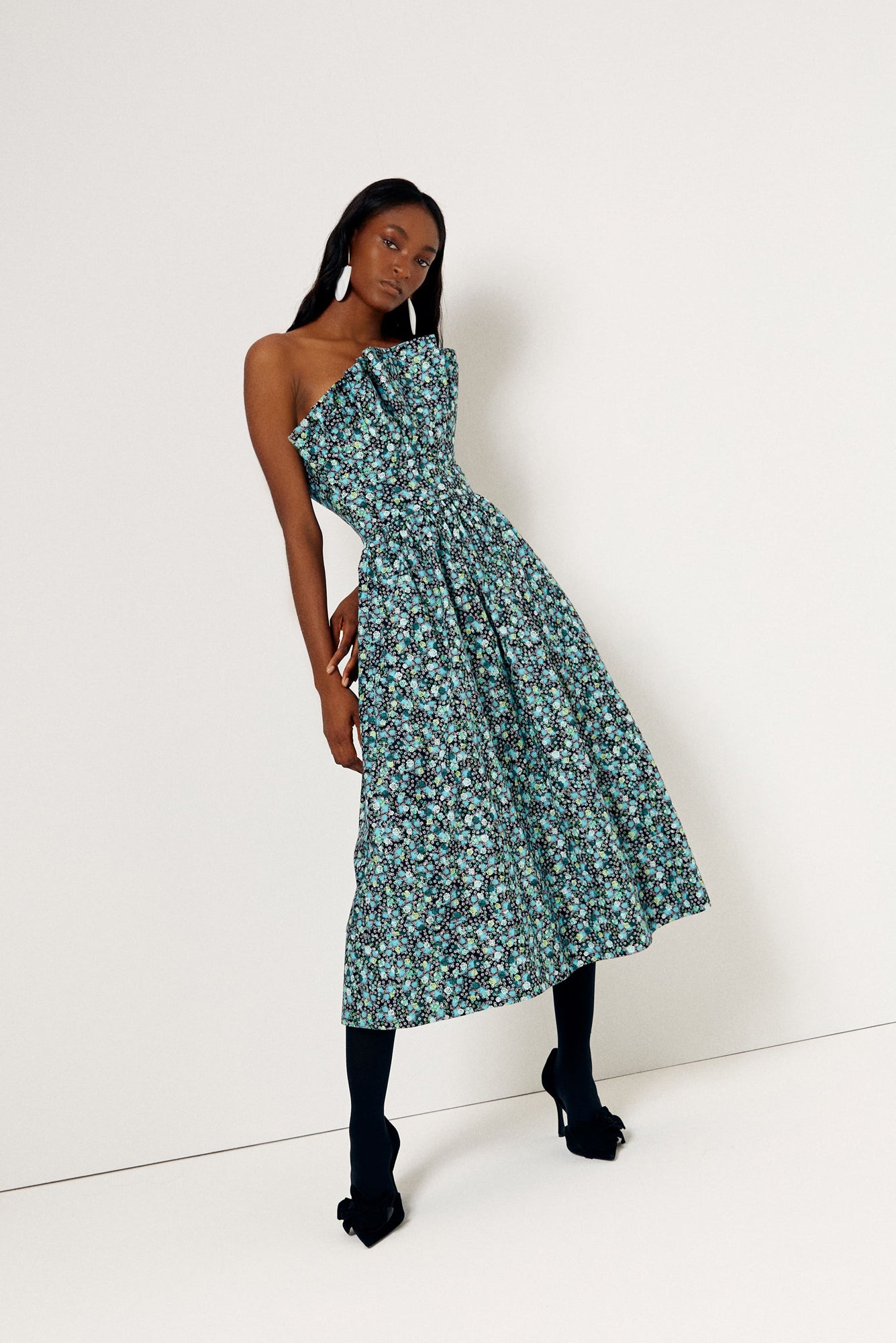 De Loreta Abanico dress in jazmin print: A midi dress with an sculptural bodice, reminiscent of delicate shells gracefully cascading over the torso. This unique design element not only adds a sense of artistry but also accentuates your silhouette, creating a flattering and eye-catching effect complemented with a blue, green and white colored floral pattern.