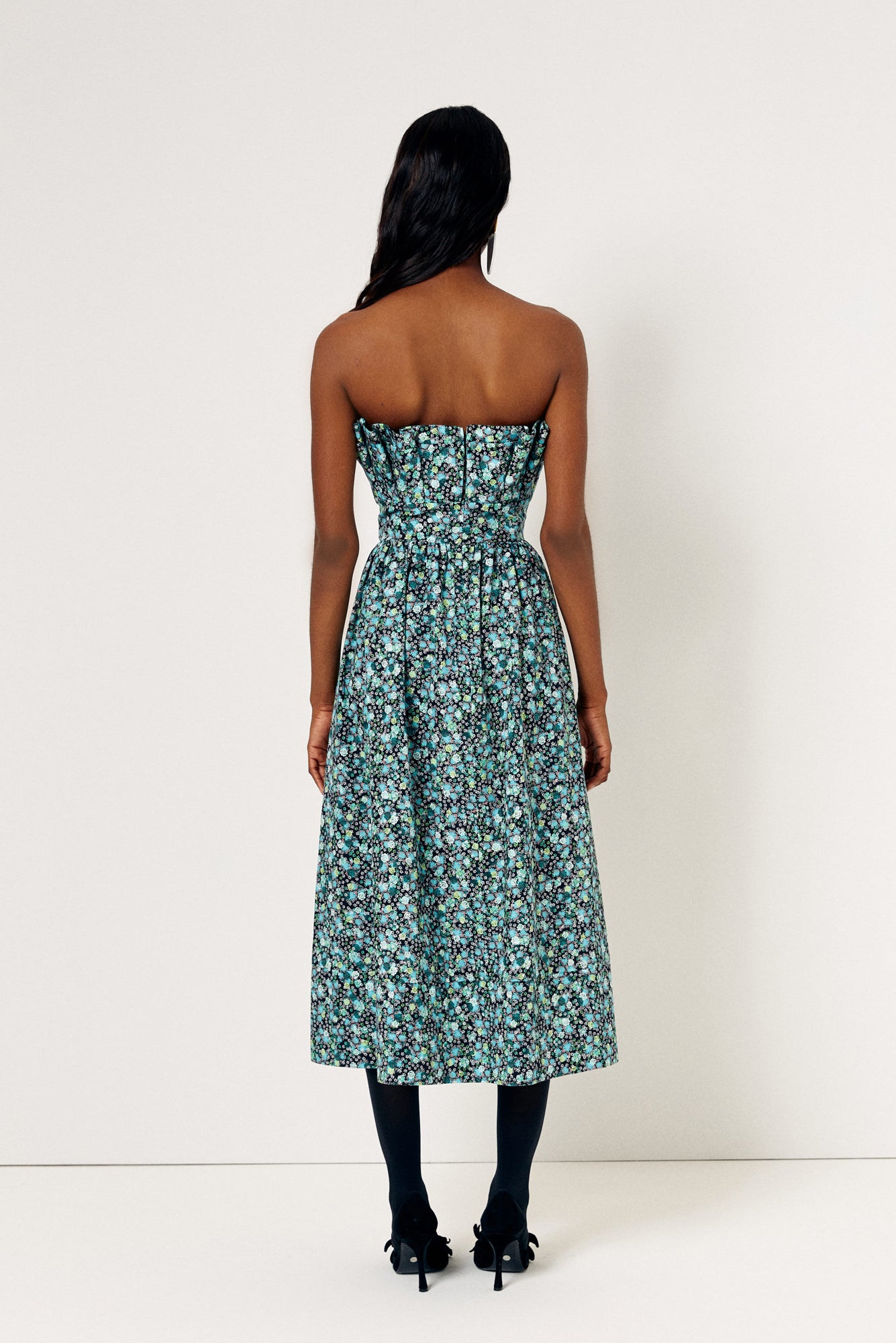 De Loreta Abanico dress in jazmin print: A midi dress with an sculptural bodice, reminiscent of delicate shells gracefully cascading over the torso. This unique design element not only adds a sense of artistry but also accentuates your silhouette, creating a flattering and eye-catching effect complemented with a blue, green and white colored floral pattern.